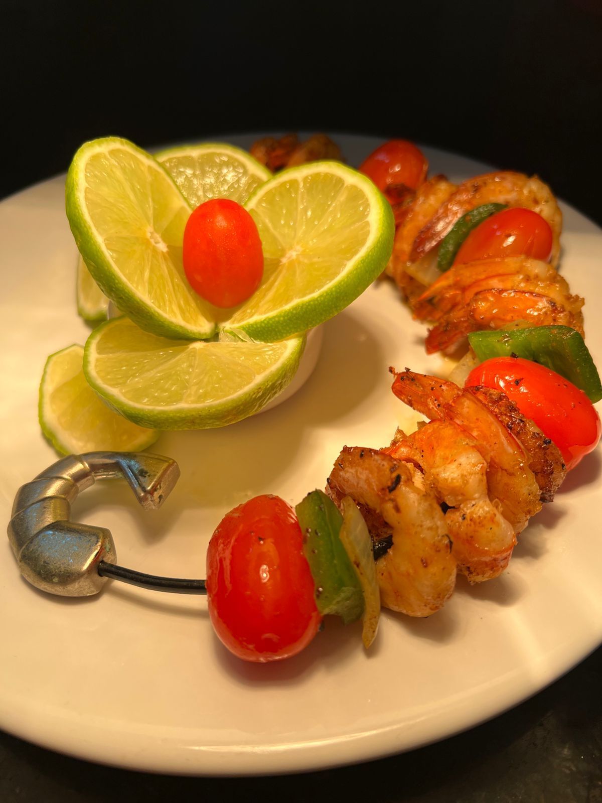 Espetos de camarão com tomates vermelhos e pimentões verdes em um prato branco, guarnecido com limão.Pousada Villa Italiana