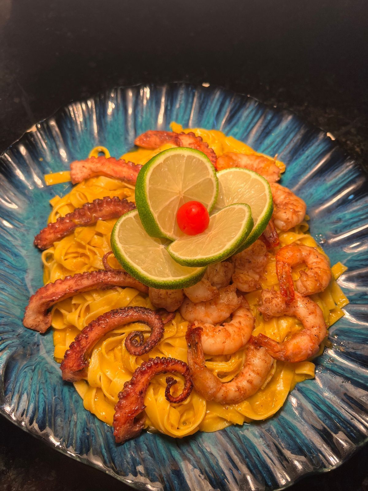 Prato de massa com polvo, camarão e guarnição de limão em um prato azul decorativo.