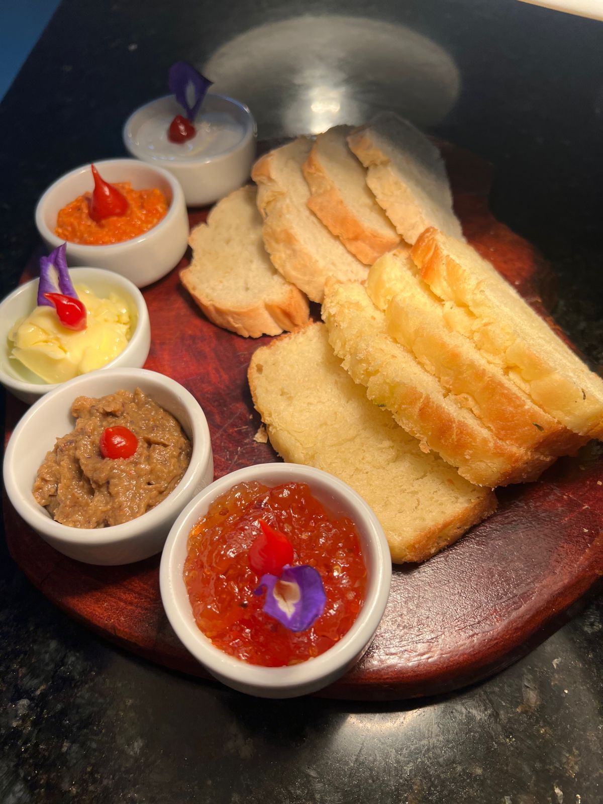 Fatias de pão com vários molhos, incluindo branco, laranja e integral, sobre uma tábua de madeira.Pousada Villa Italiana
