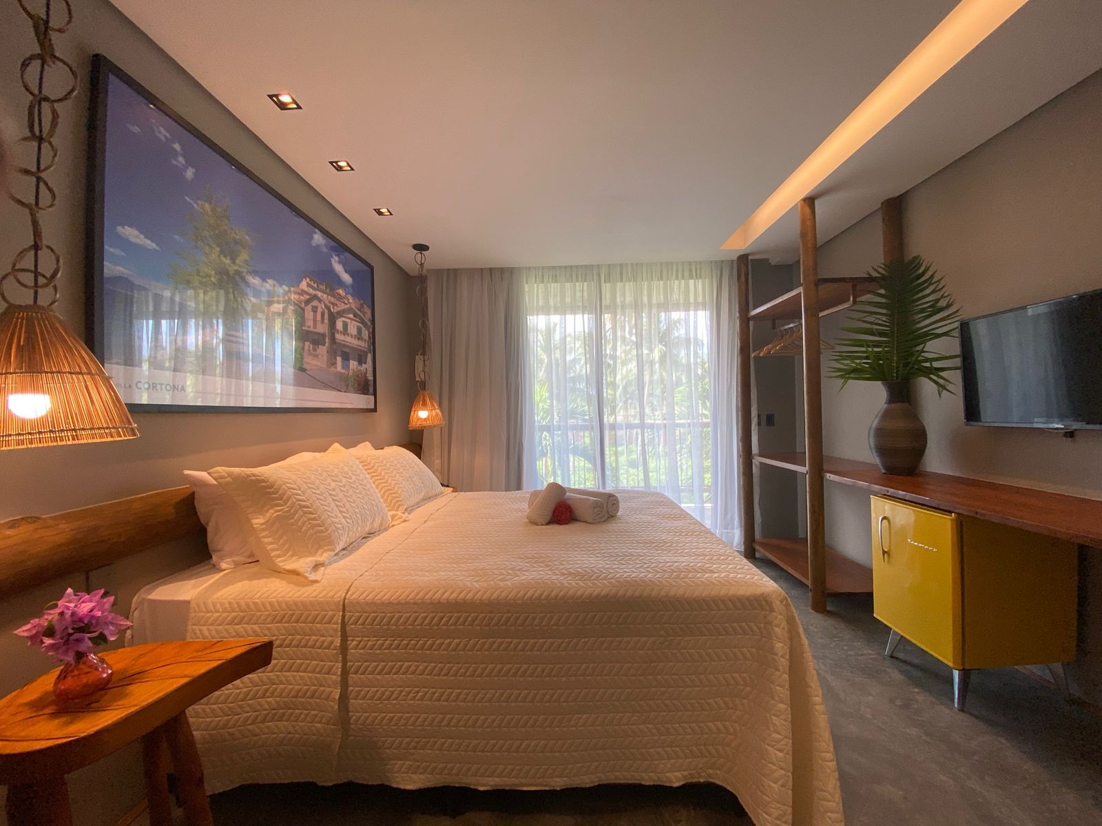 Quarto com cama king-size, roupa de cama de cor clara e um armário amarelo sob uma TV montada.Pousada Villa Italiana