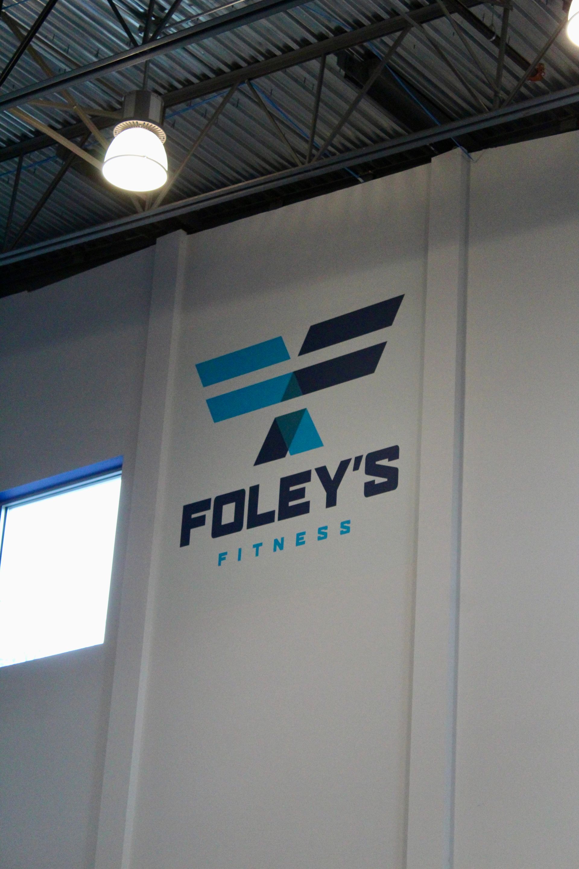 Foley's Fitness logo on a white wall; blue and dark blue graphic, the words 