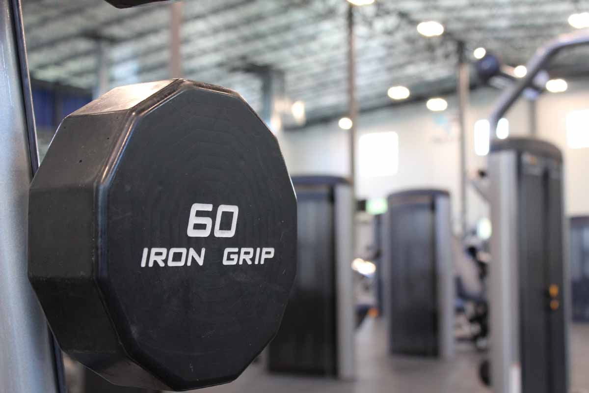 Black 60 lb Iron Grip dumbbell in a gym. Other weight machines in the background.