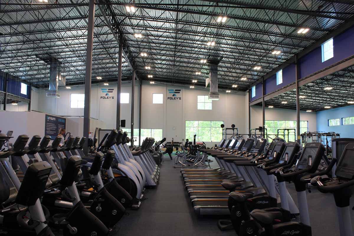 Rows of exercise equipment in a brightly lit gym. Treadmills, bikes, and weight machines.