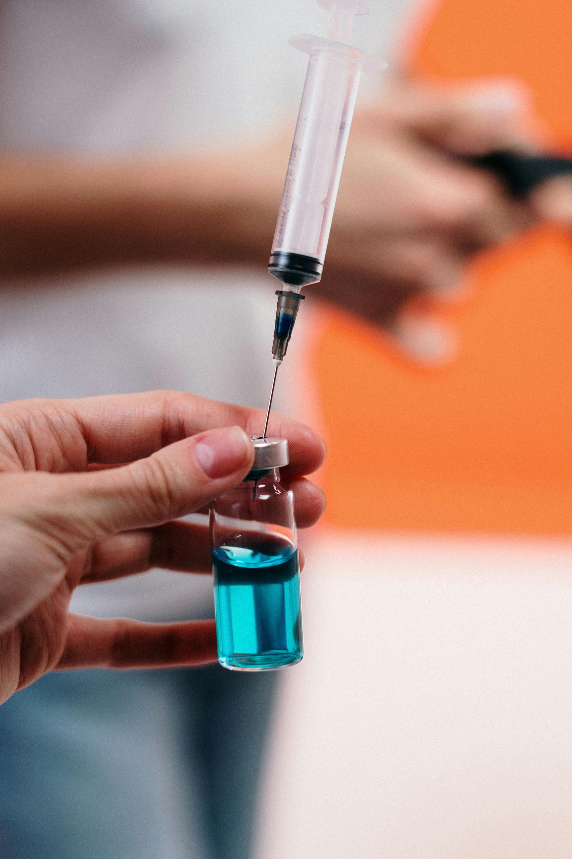 A person is holding a syringe and a bottle of blue liquid.