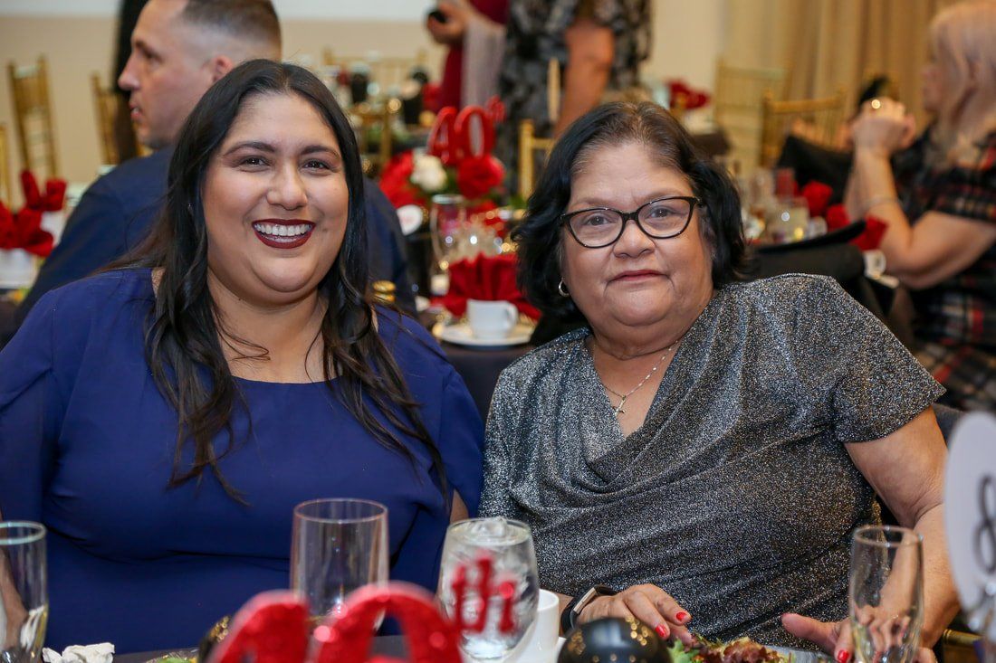 Two women are posing for a picture while sitting at a table at a party.