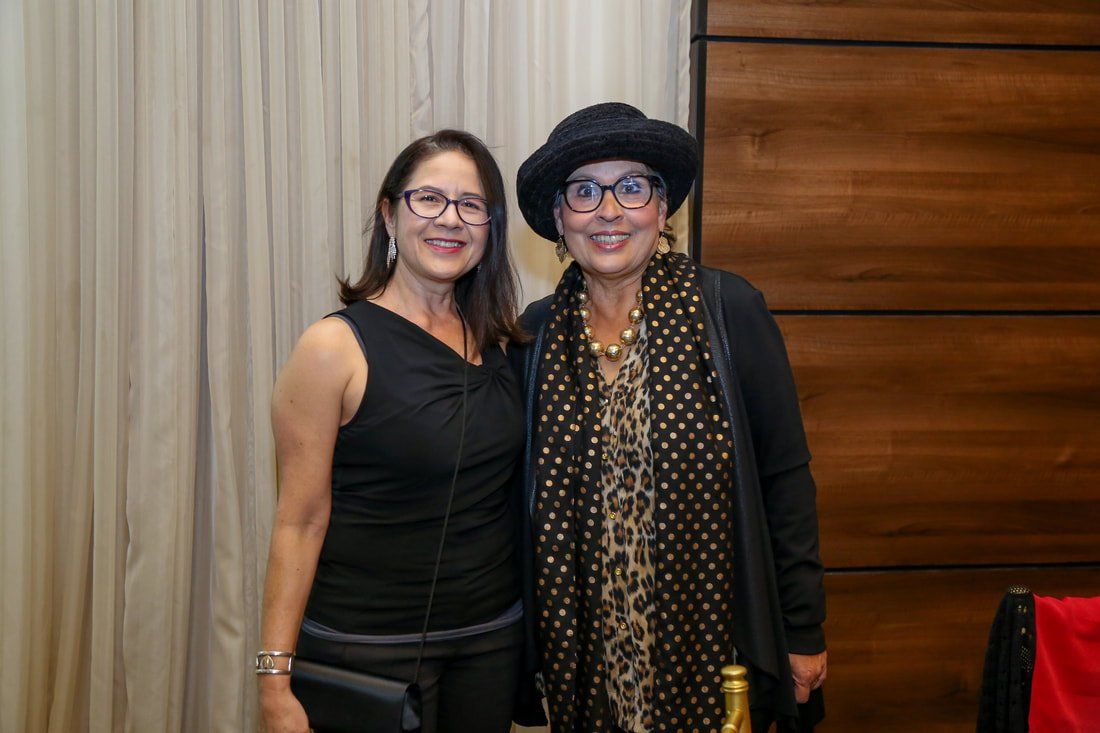 Two women are posing for a picture together in front of a wooden wall.