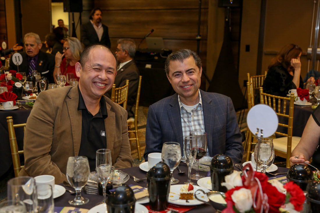 Two men are sitting at a table with wine glasses and smiling.