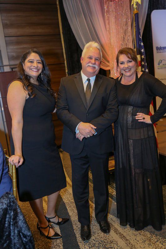 A man in a suit and tie is standing next to two women in black dresses.