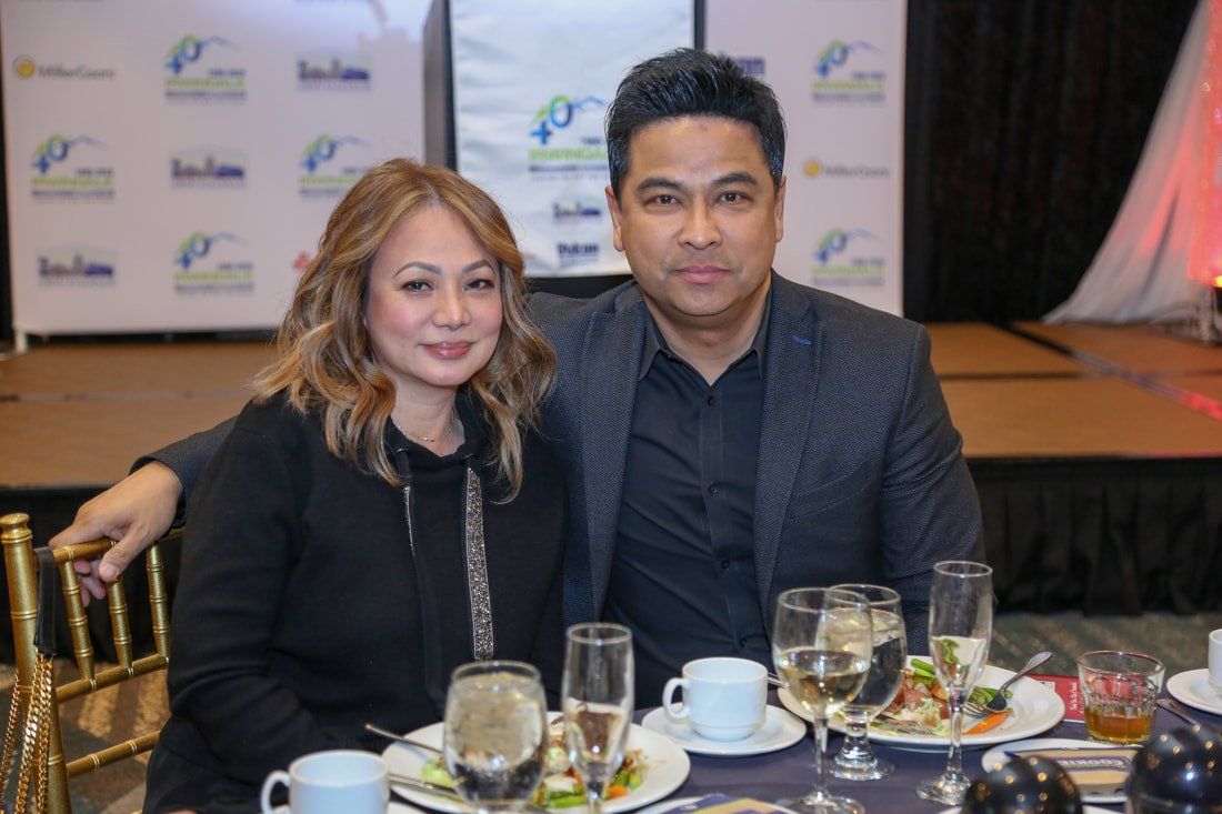 A man and a woman are sitting at a table with plates of food and wine glasses.
