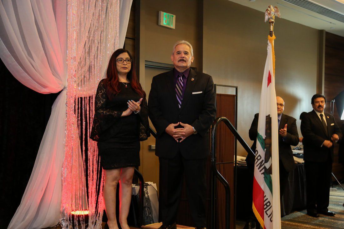 A man and a woman are standing in front of a flag.