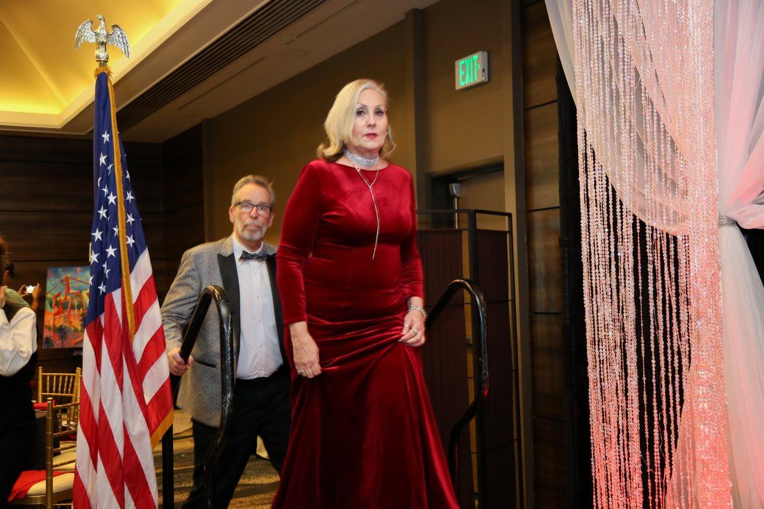 A woman in a red dress is walking down a staircase next to an american flag.