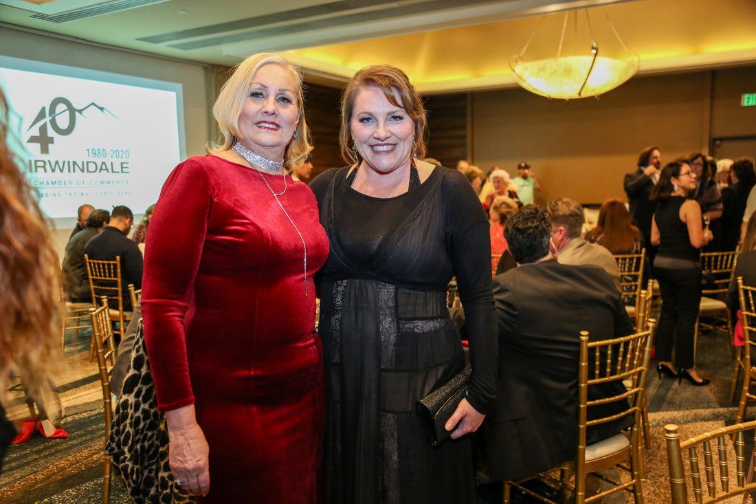 Two women are standing next to each other in a room at a party.