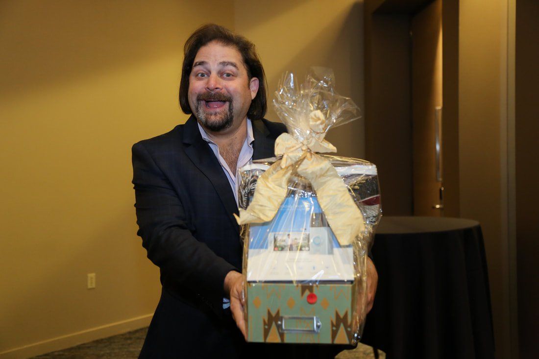 A man in a suit is holding a gift basket wrapped in plastic.