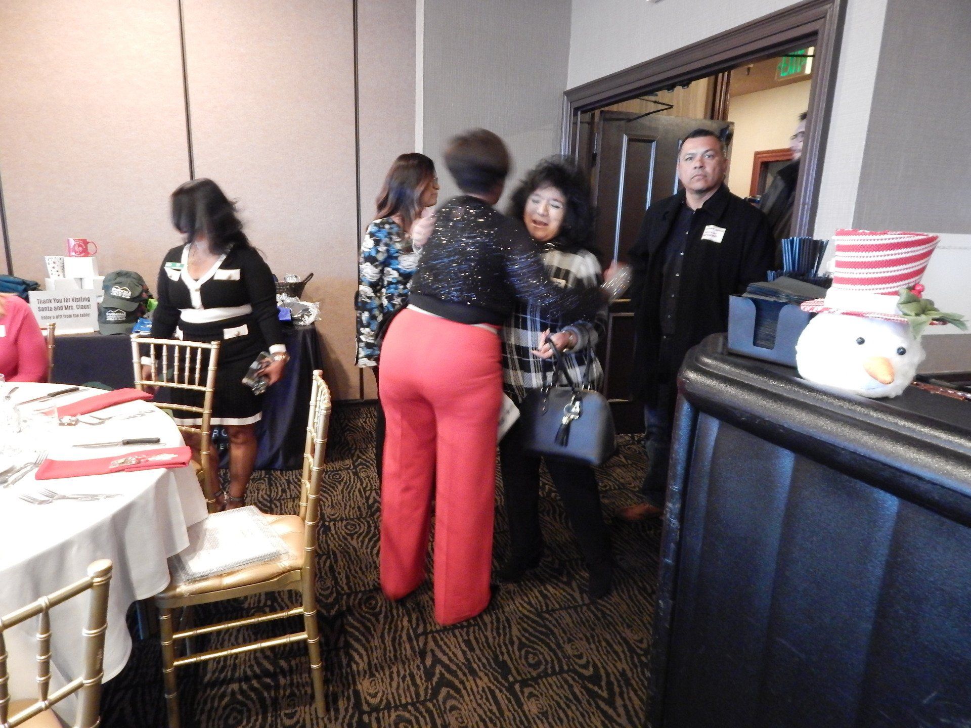 A group of people are standing in a room with tables and chairs.