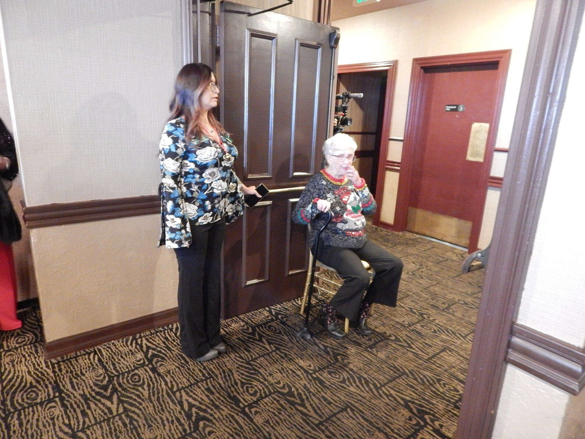 A woman is standing next to a woman in a wheelchair in a hallway.