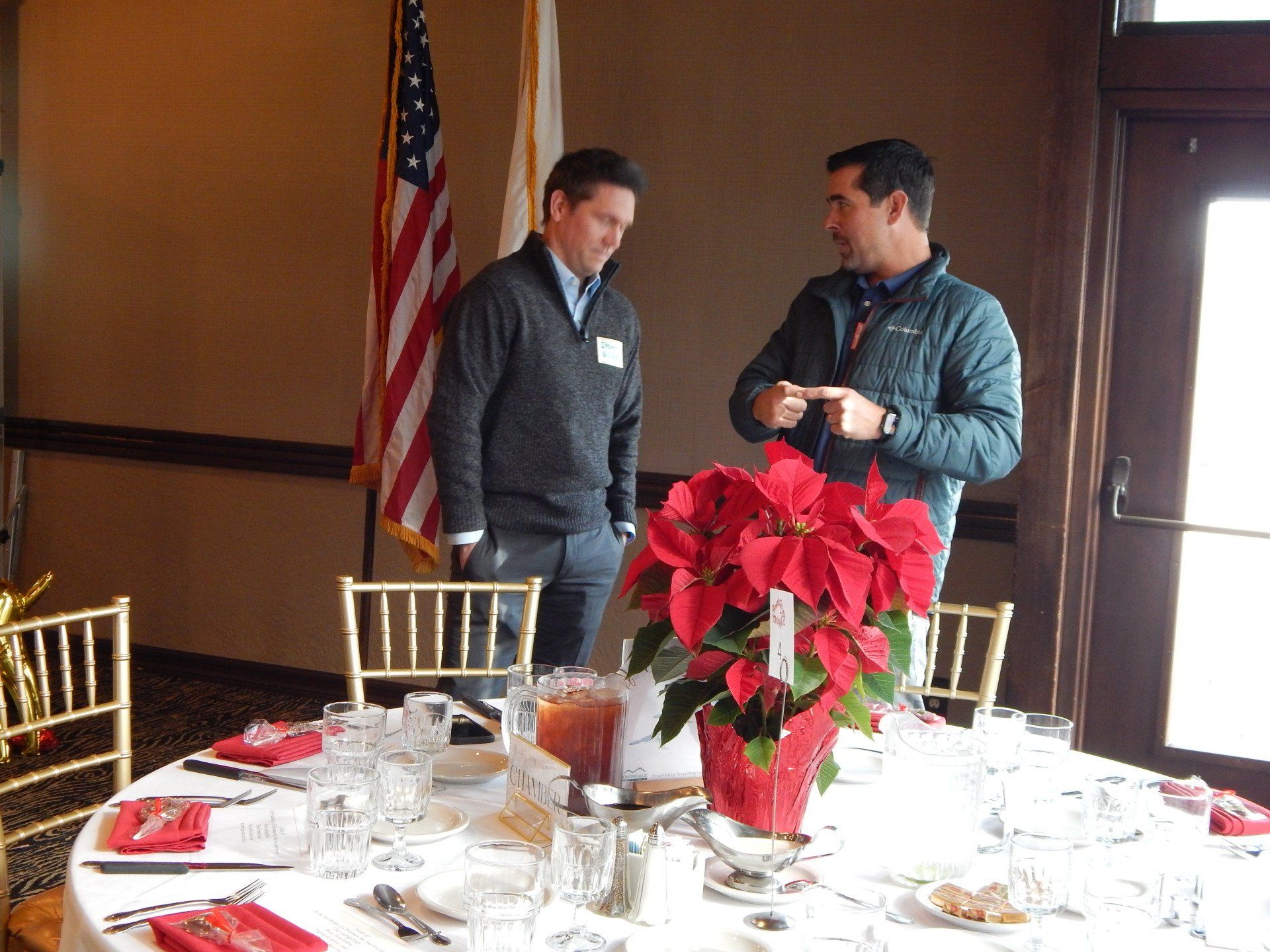 Two men are standing in front of a table with a poinsettia on it.