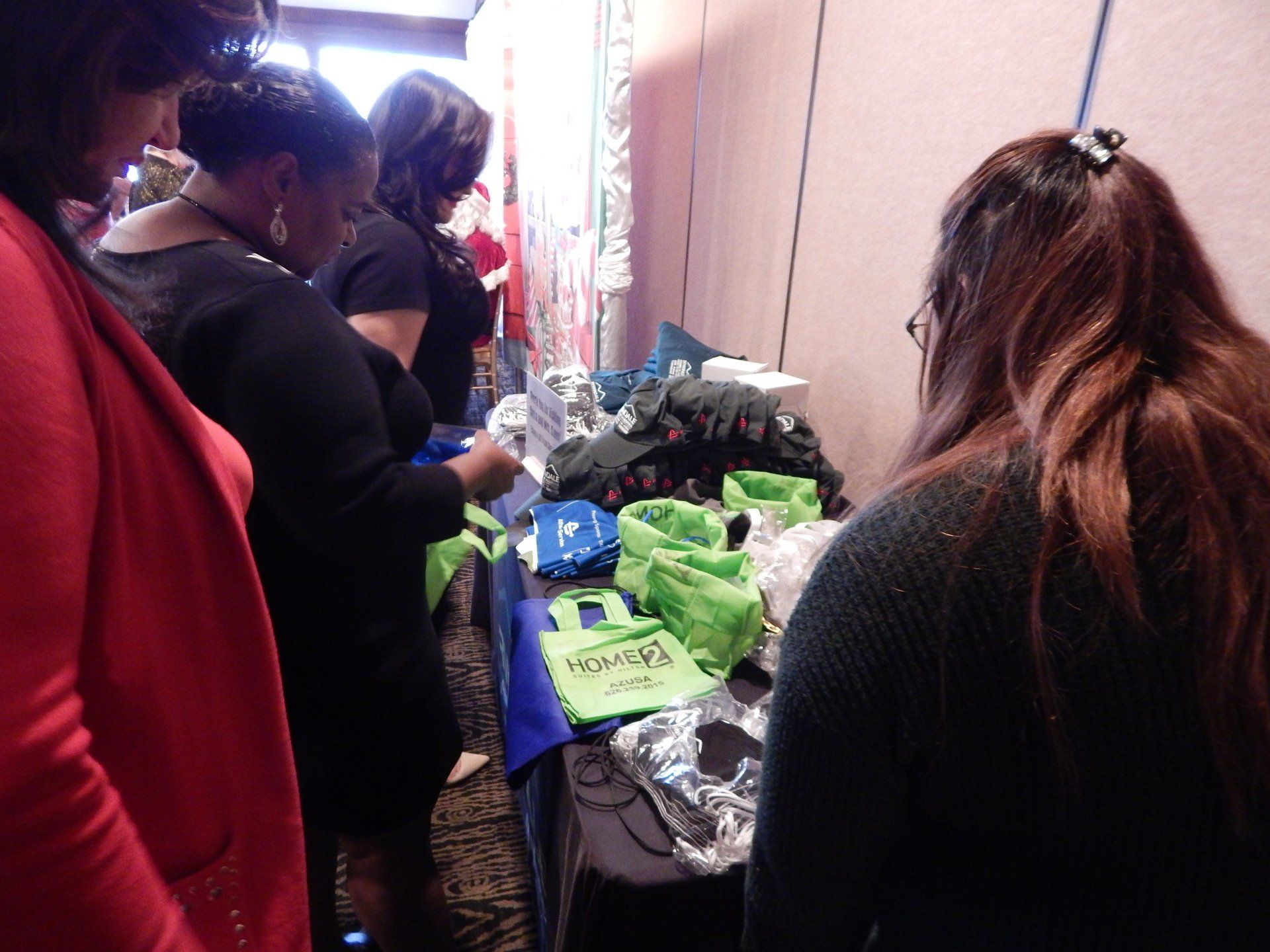 A group of women are standing around a table with a green bag that says ' hawaii ' on it