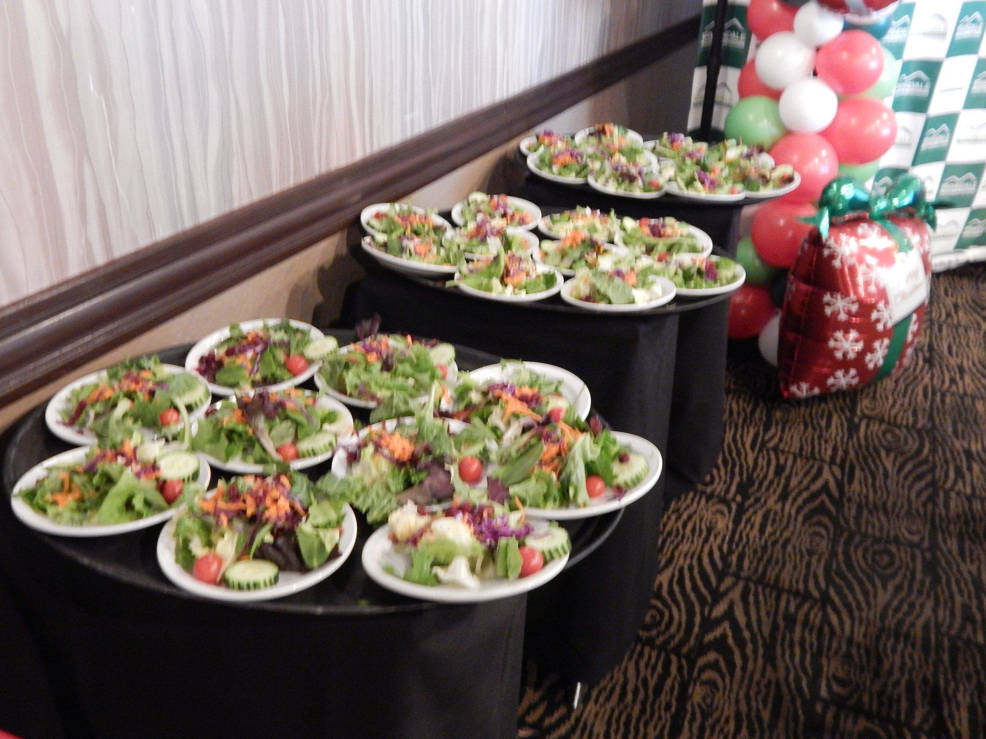 A bunch of salads on a table with balloons in the background