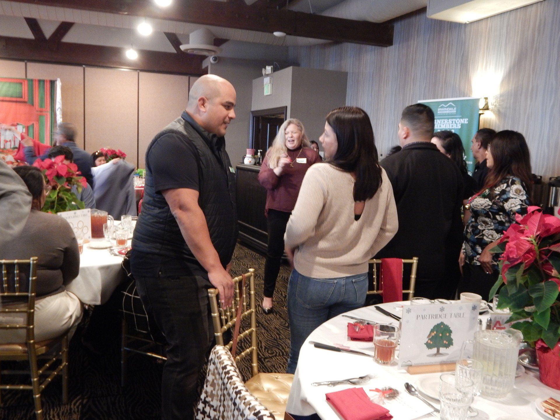 A group of people are standing around tables in a room talking to each other.