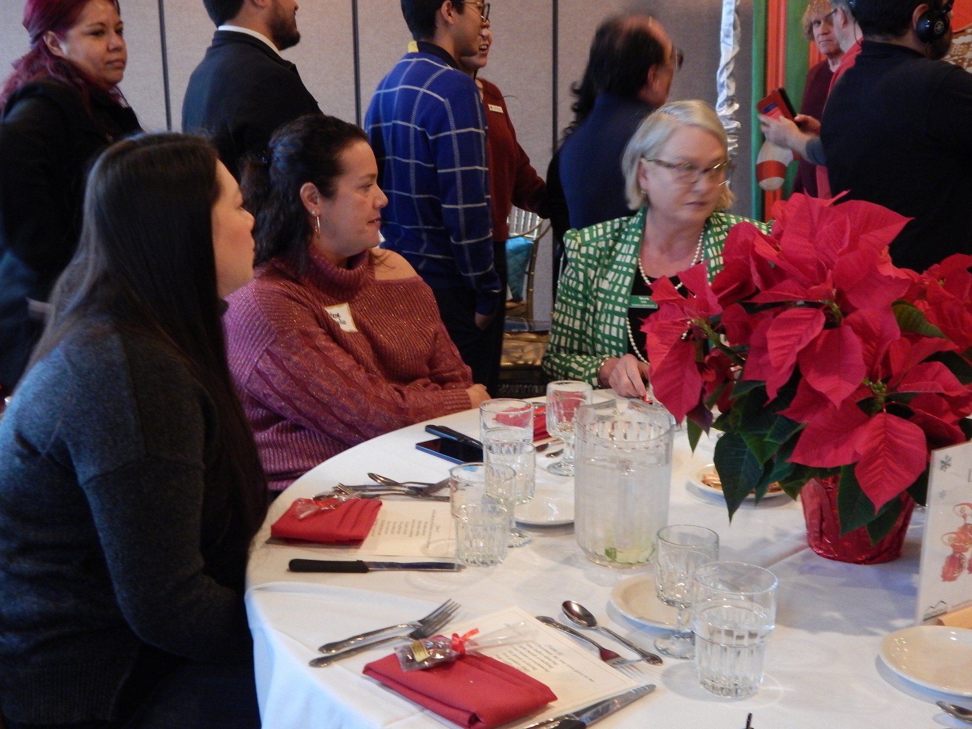 A group of people are sitting at a table with a poinsettia in front of them.