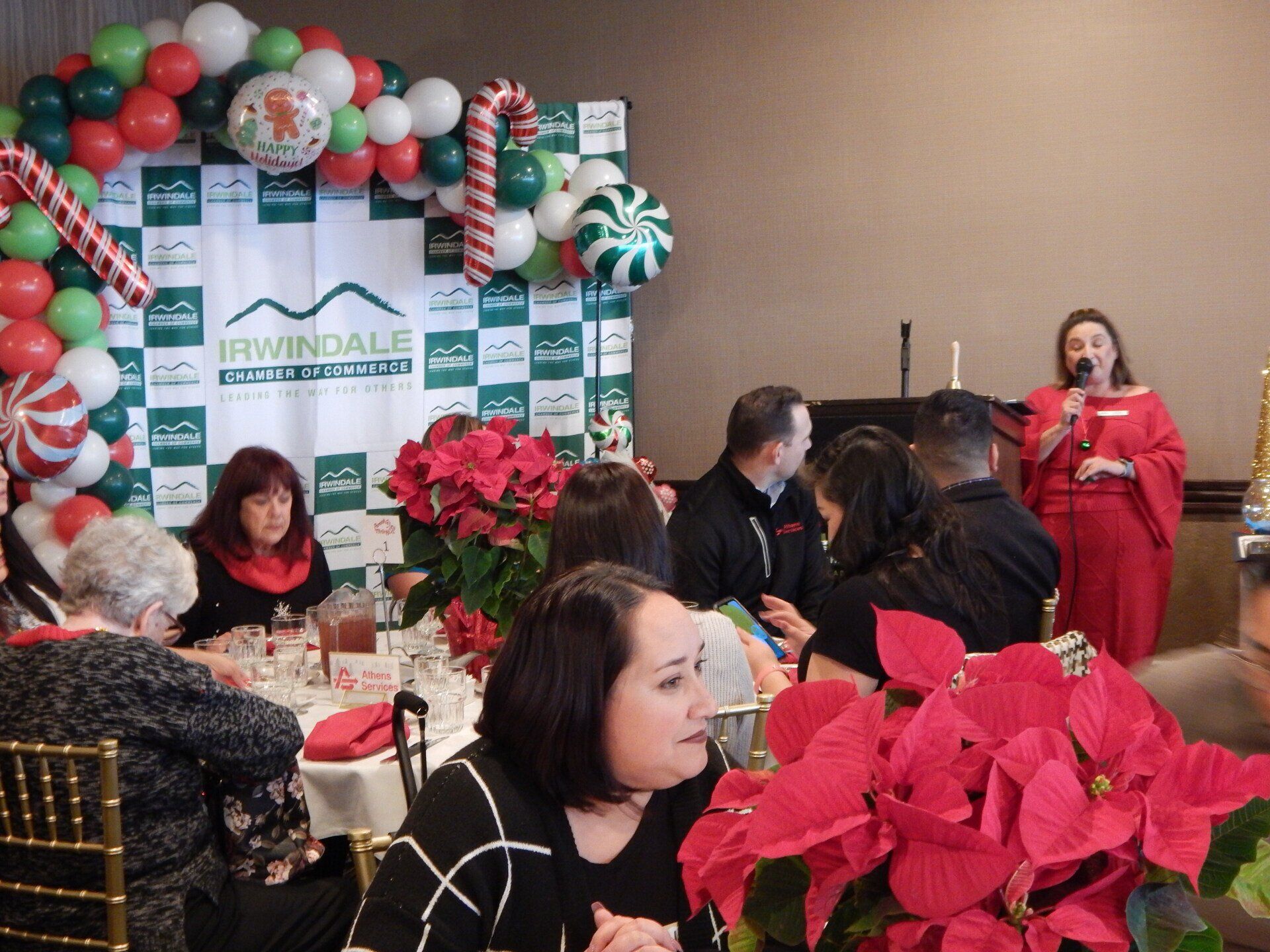 A group of people are sitting at tables in front of a christmas backdrop.