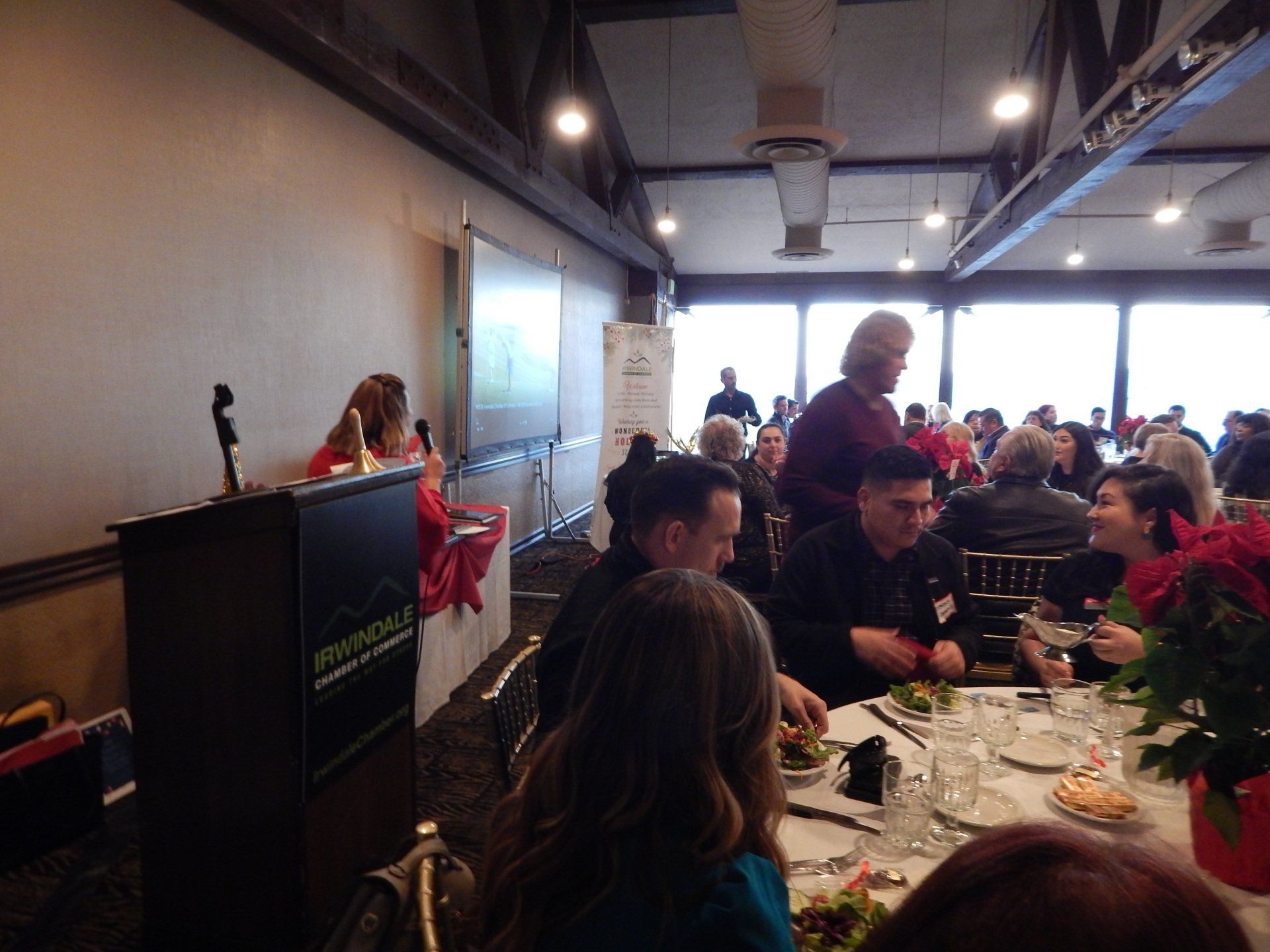 A woman is giving a speech to a large group of people at a dinner table.