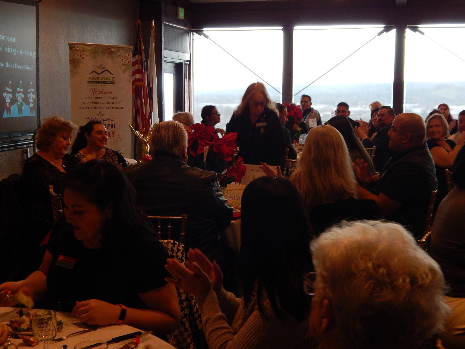 A group of people are sitting at tables in front of a large window.
