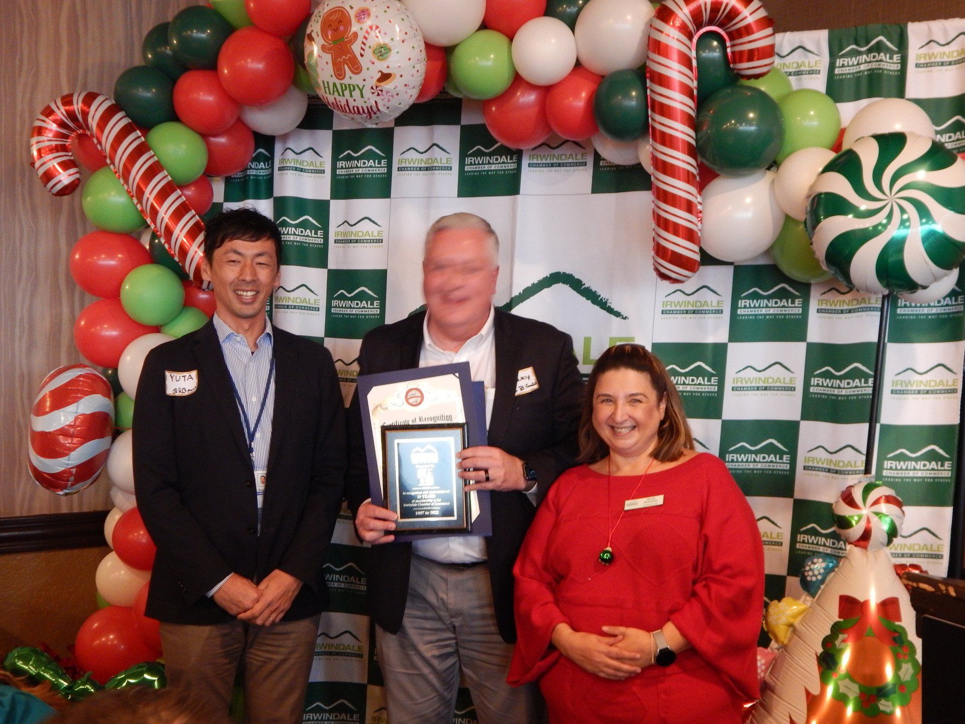 A man and two women are standing in front of a balloon arch.