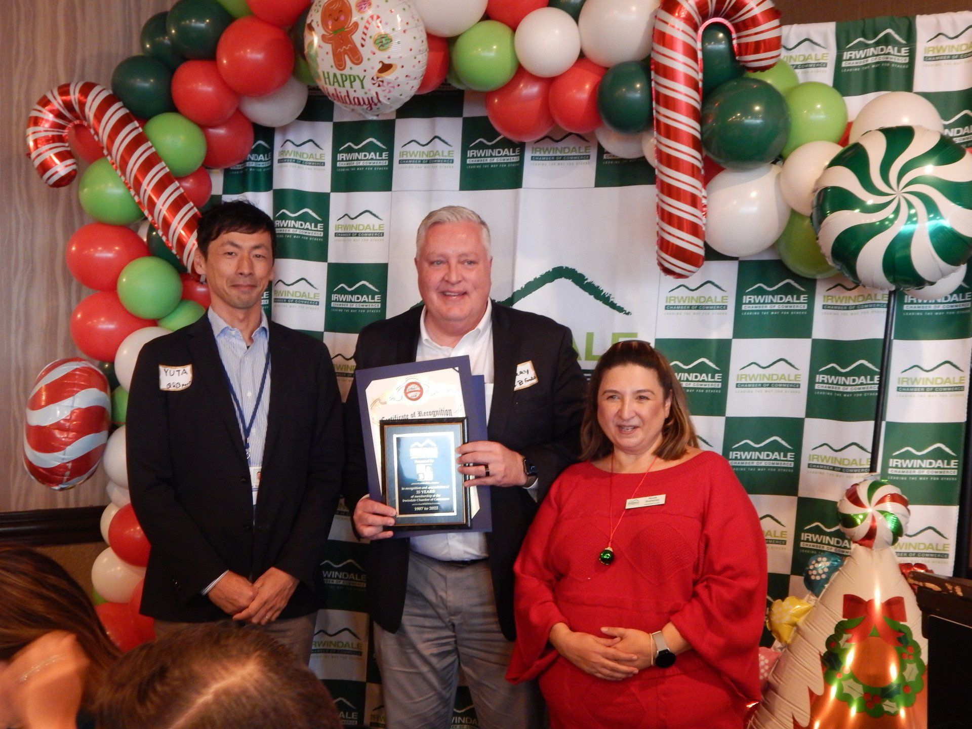 Three people are posing for a picture in front of a christmas backdrop.