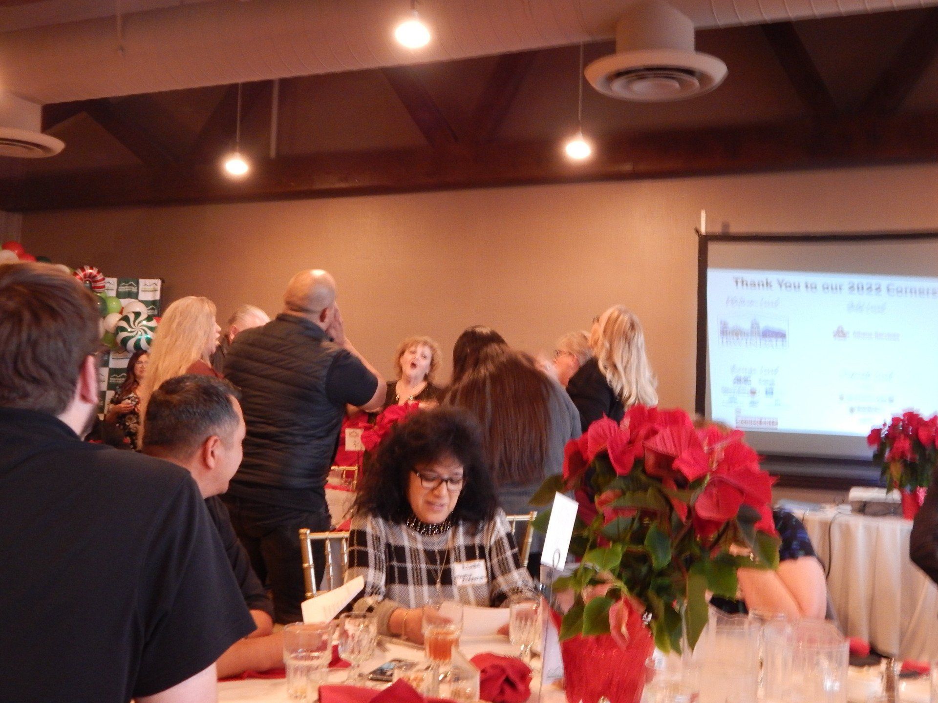 A group of people are sitting at tables in front of a projector screen.