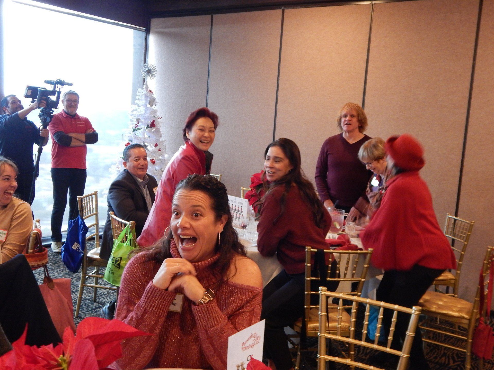 A group of people are sitting at a table with a christmas tree in the background.
