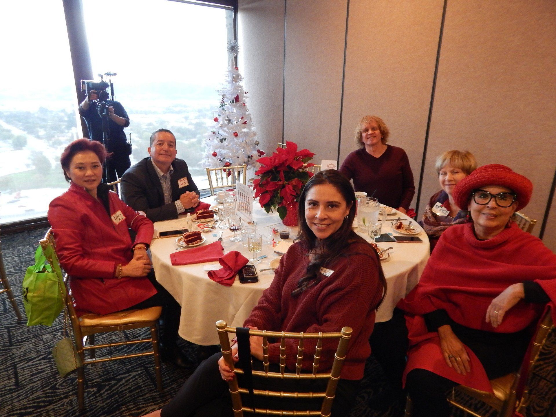 A group of people are sitting at a table with a christmas tree in the background.