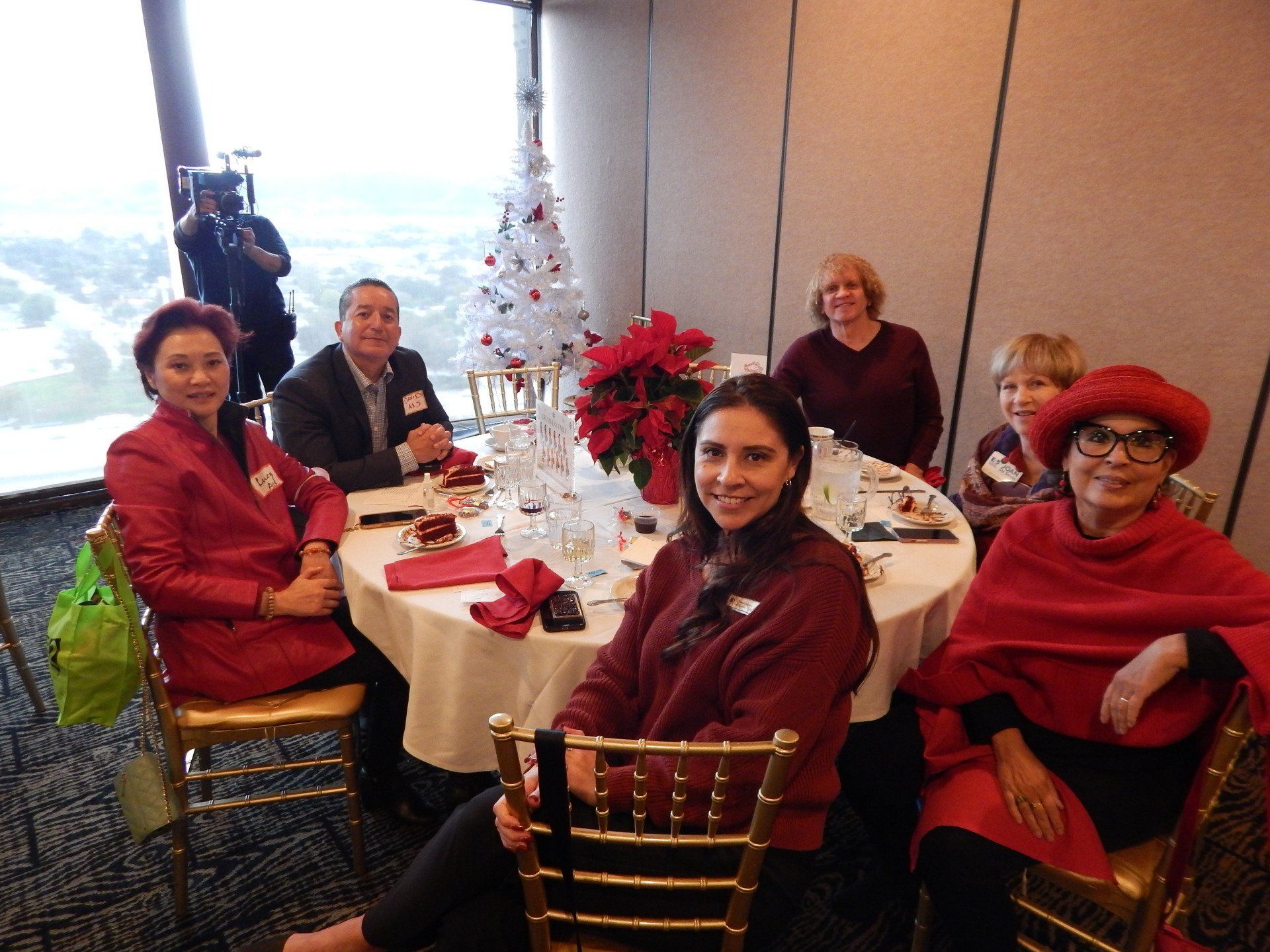 A group of people are sitting at a table with a christmas tree in the background.
