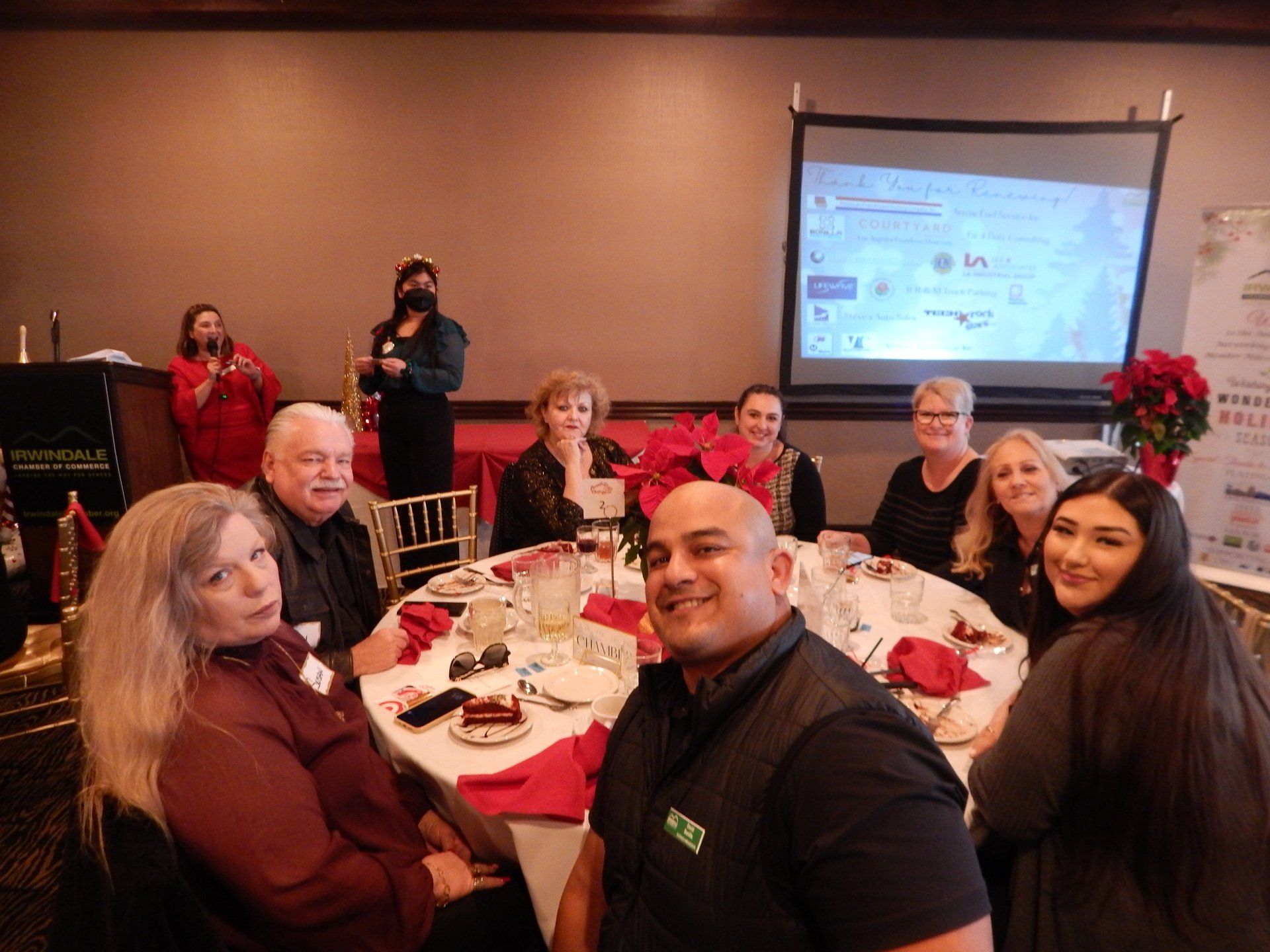 A group of people are sitting at a table in front of a projector screen.