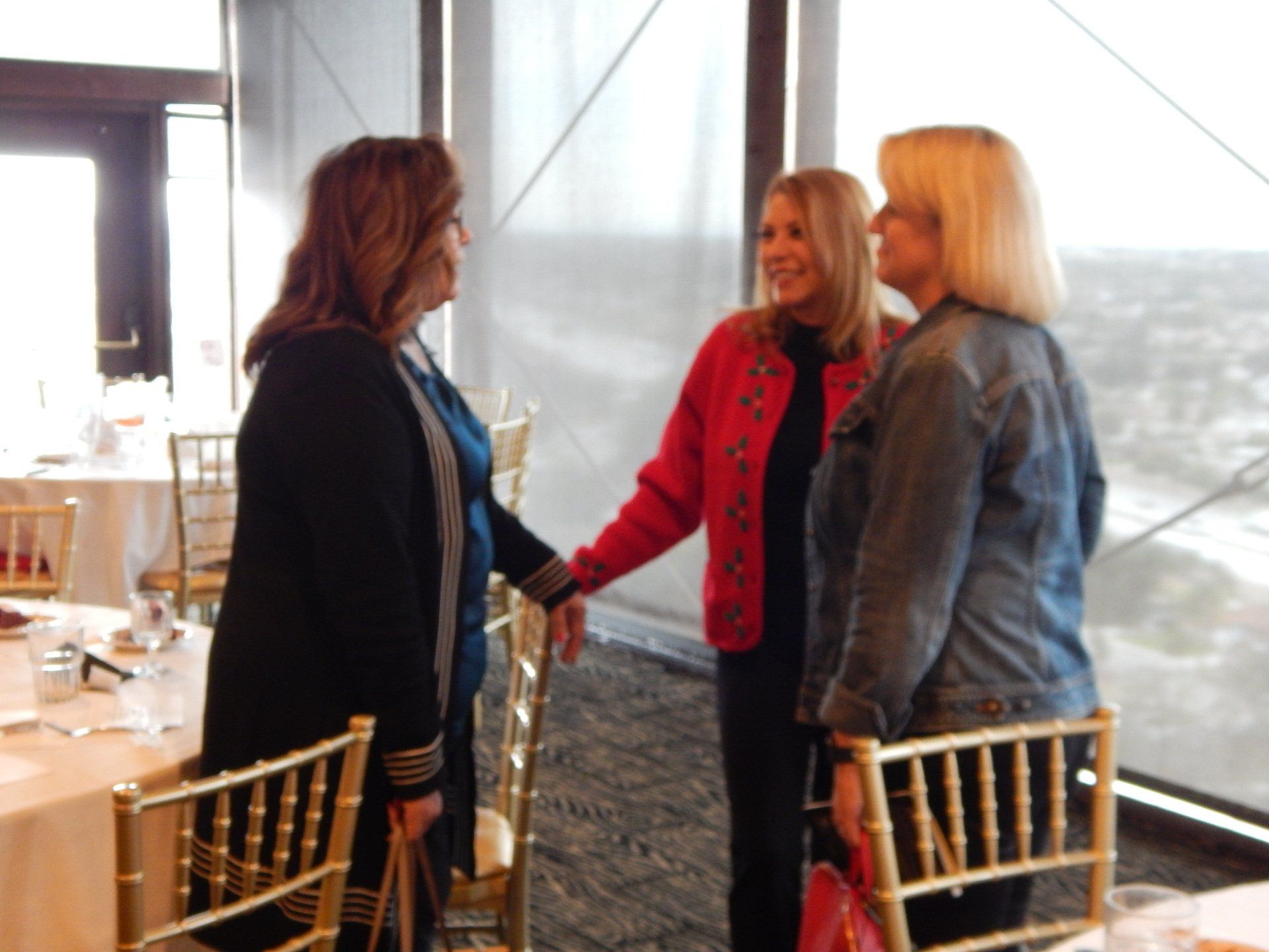 Three women are standing in front of a window talking to each other