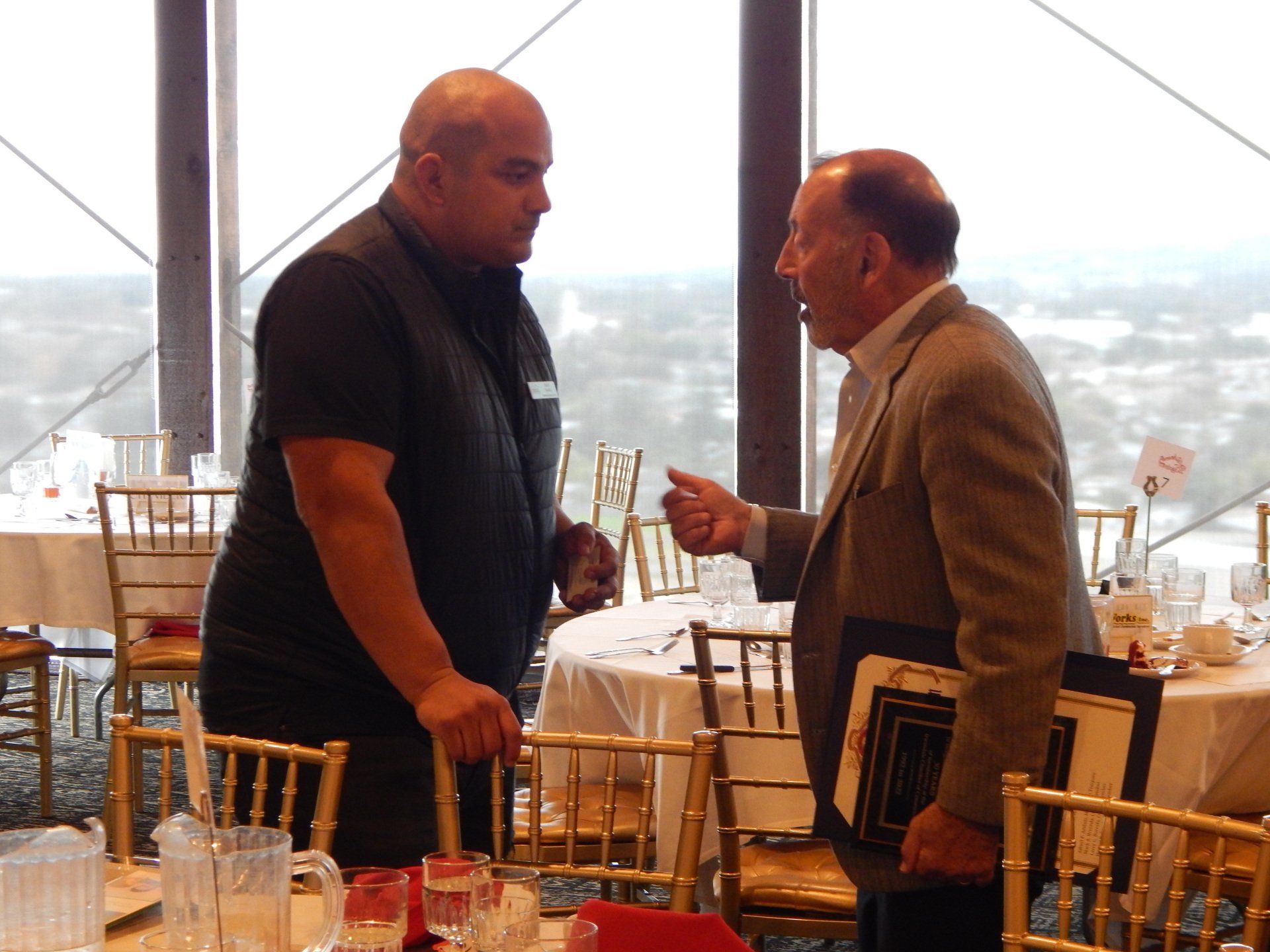 Two men are having a conversation in a room with tables and chairs