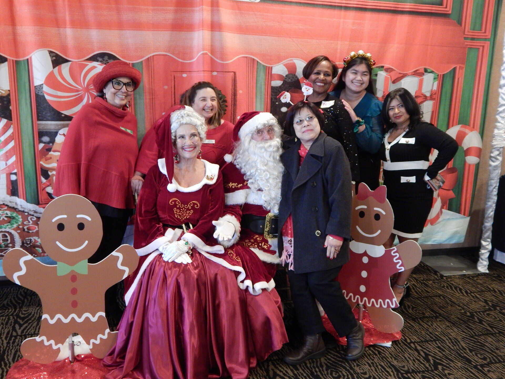 A group of women are posing for a picture with santa claus and gingerbread men.