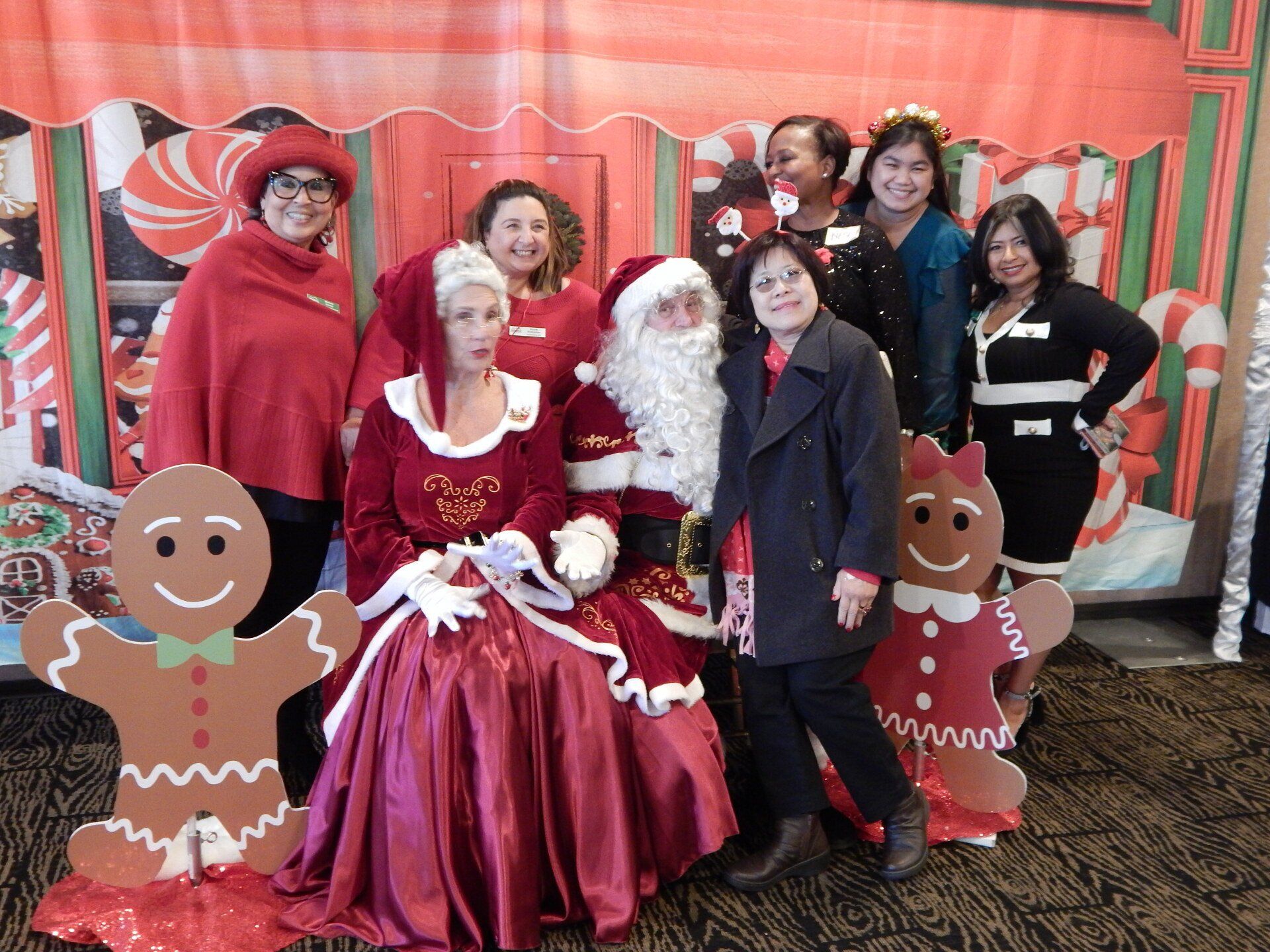A group of women are posing for a picture with santa claus and gingerbread men.