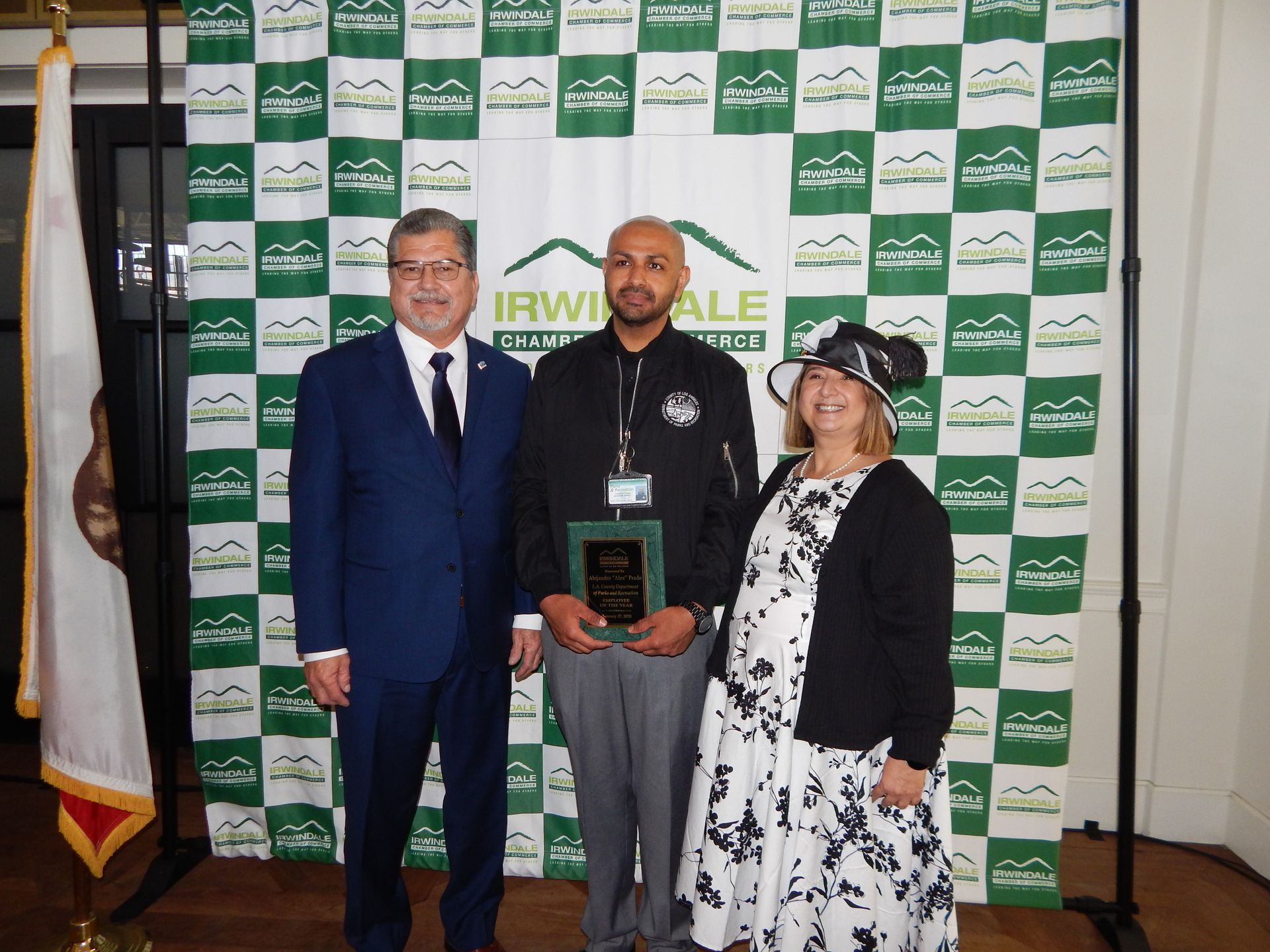 A group of people standing in front of a green and white checkered backdrop that says irwinale