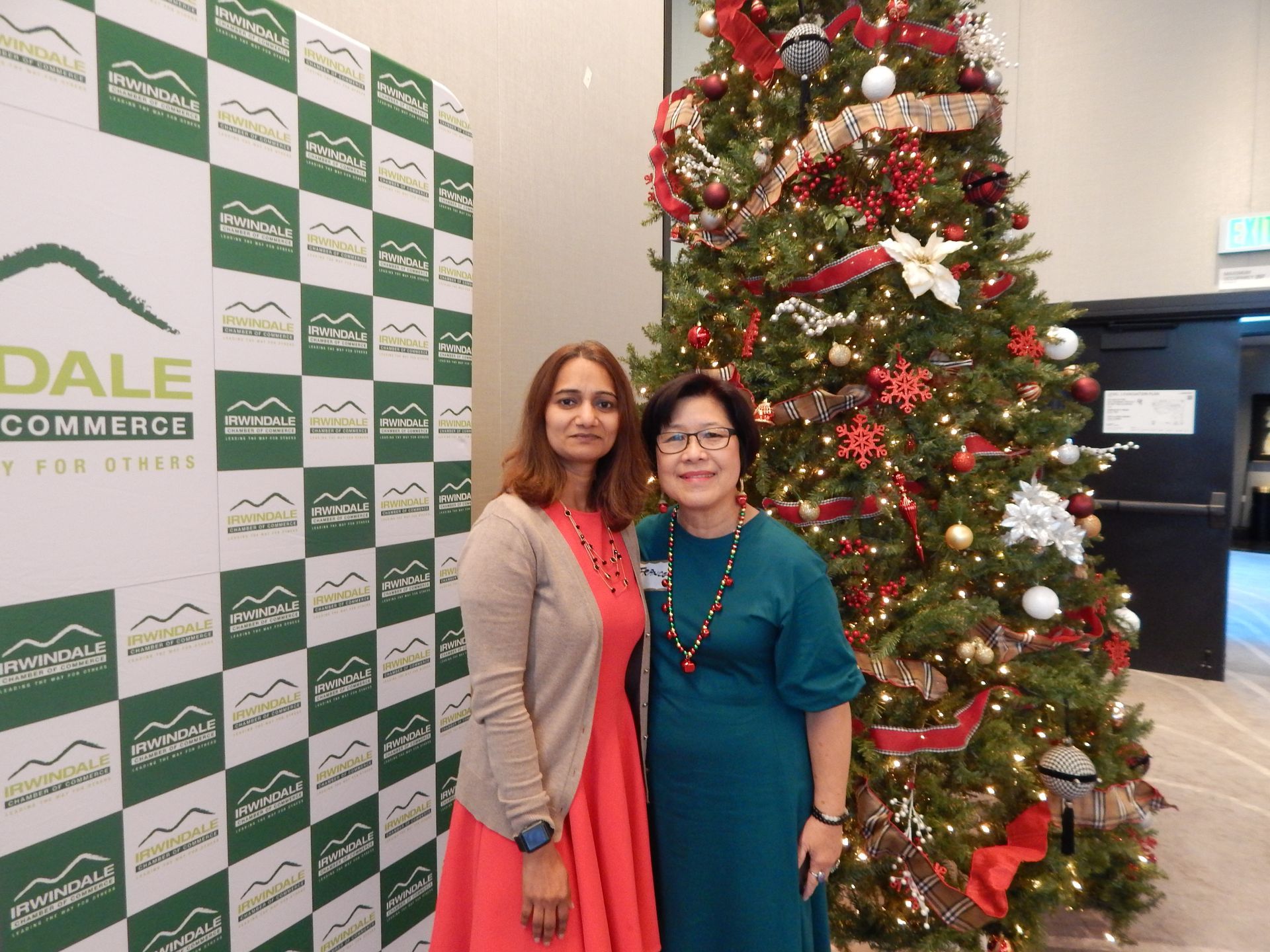 Two women are posing for a picture in front of a christmas tree.