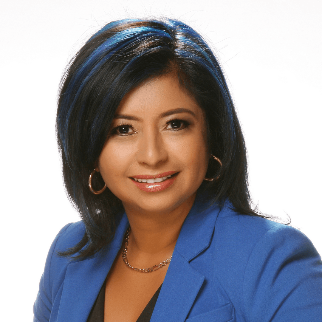 A woman wearing a blue jacket and earrings smiles for the camera