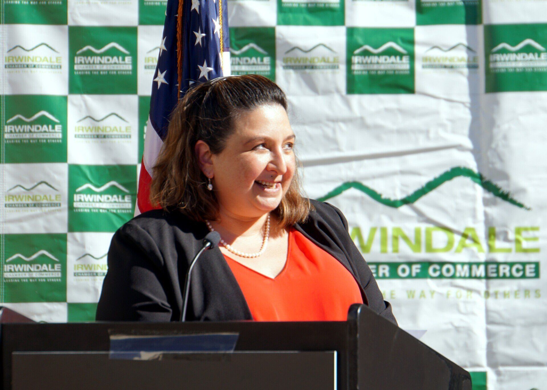 A woman is standing at a podium with an american flag in the background.