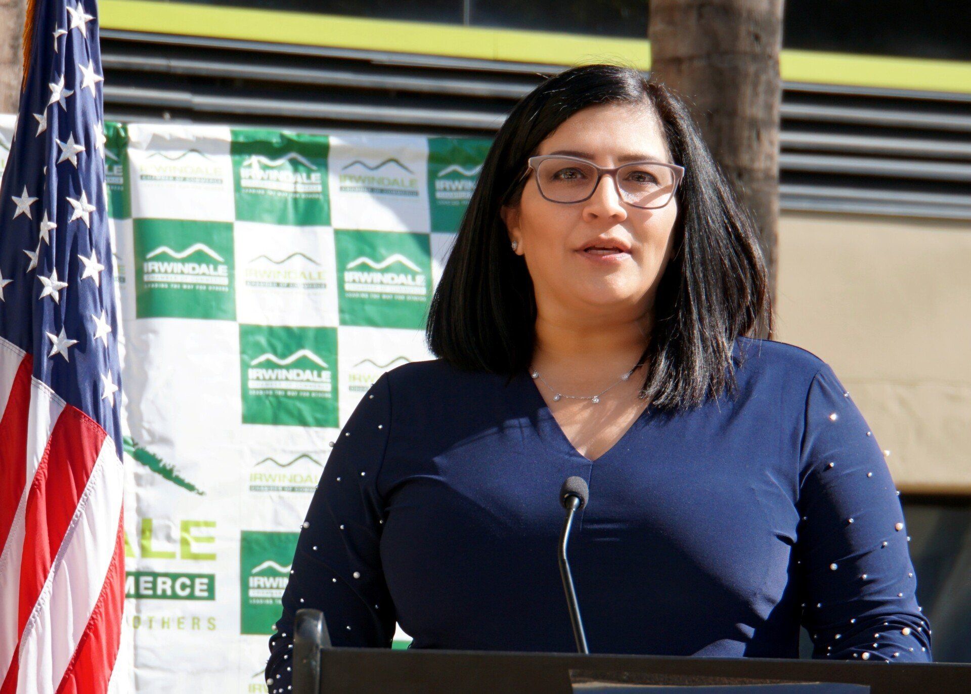 A woman is standing at a podium in front of an american flag.