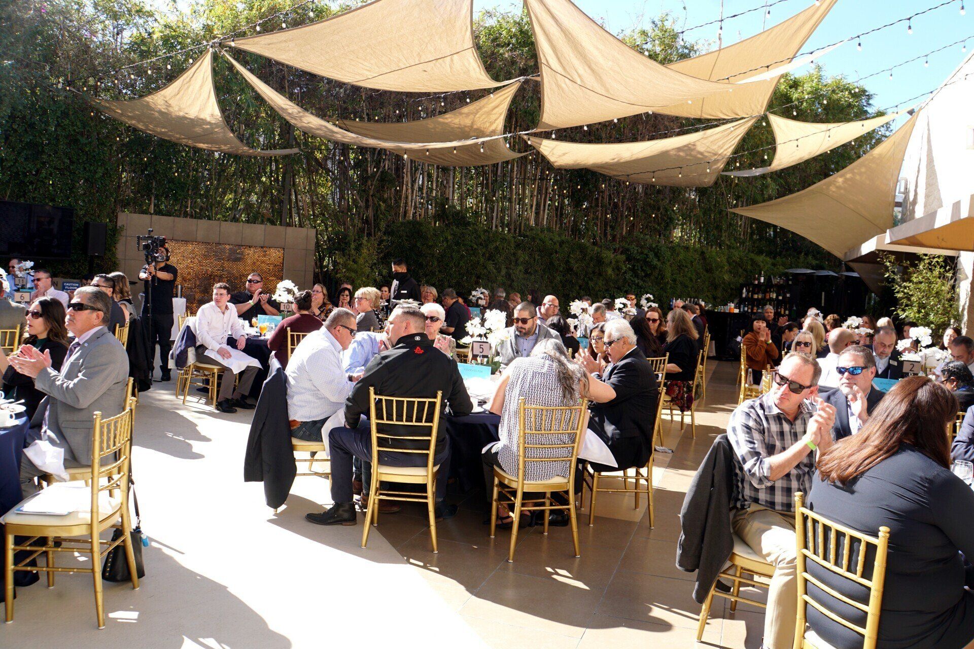 A large group of people are sitting at tables under umbrellas