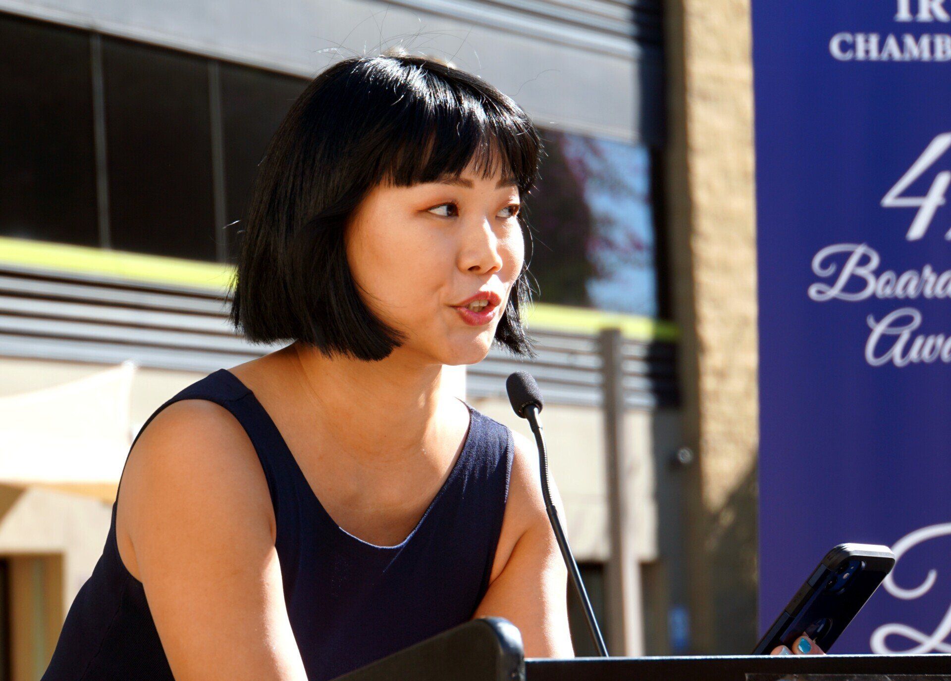 A woman speaking into a microphone in front of a sign that says 4 board awards