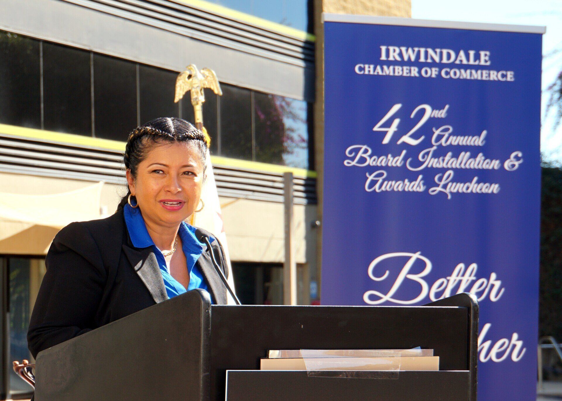 A woman stands at a podium in front of a sign that says better her
