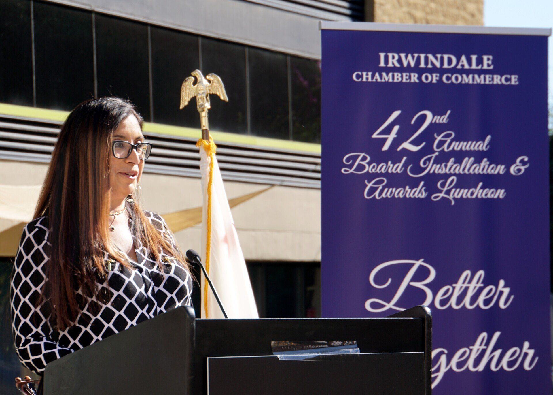 A woman stands at a podium in front of a sign that says better together