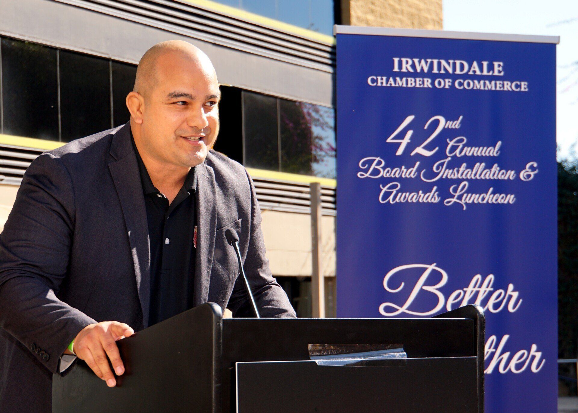 A man stands at a podium in front of a sign that says better her