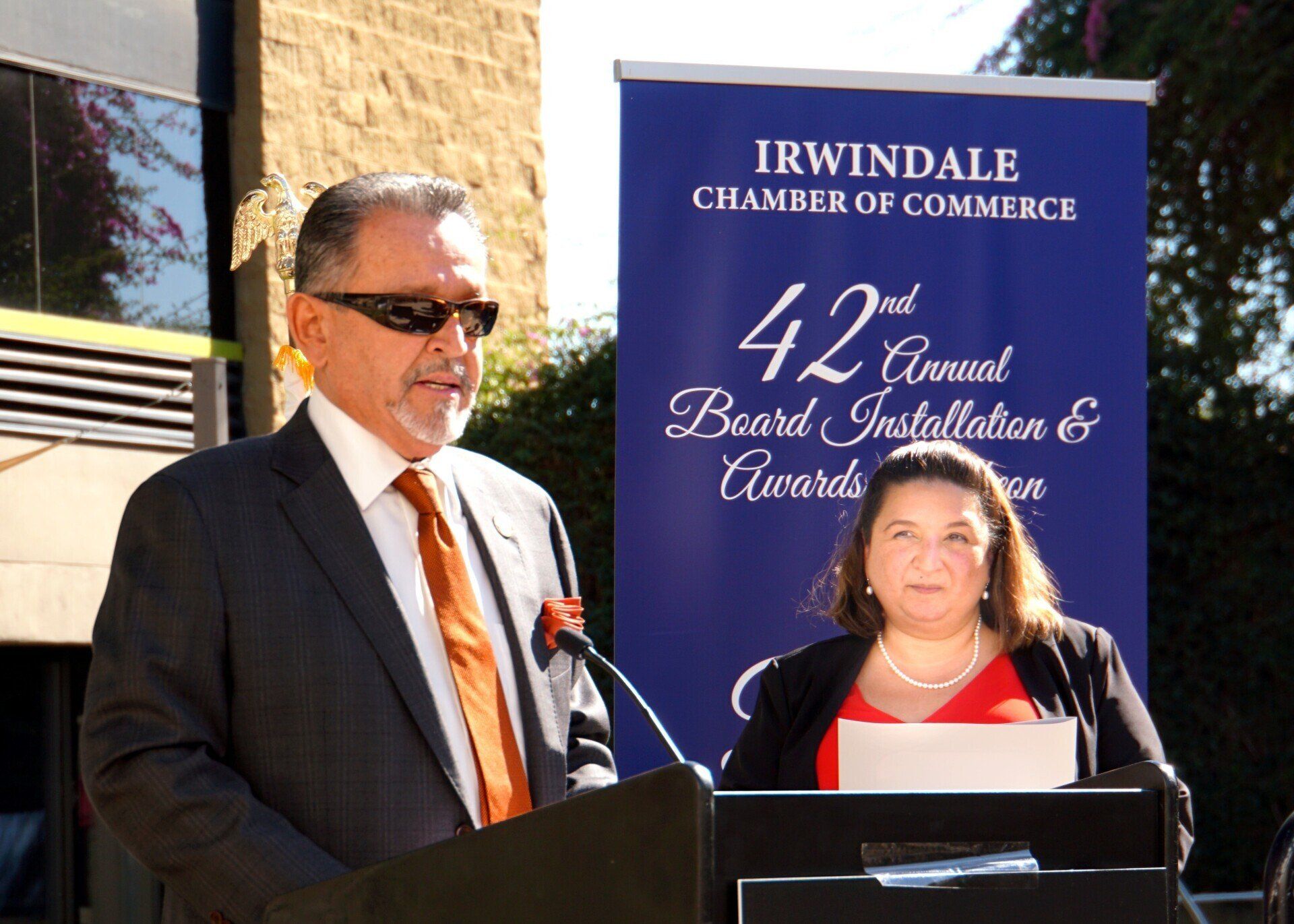 A man in a suit and tie is giving a speech in front of a sign that says irwindale chamber of commerce