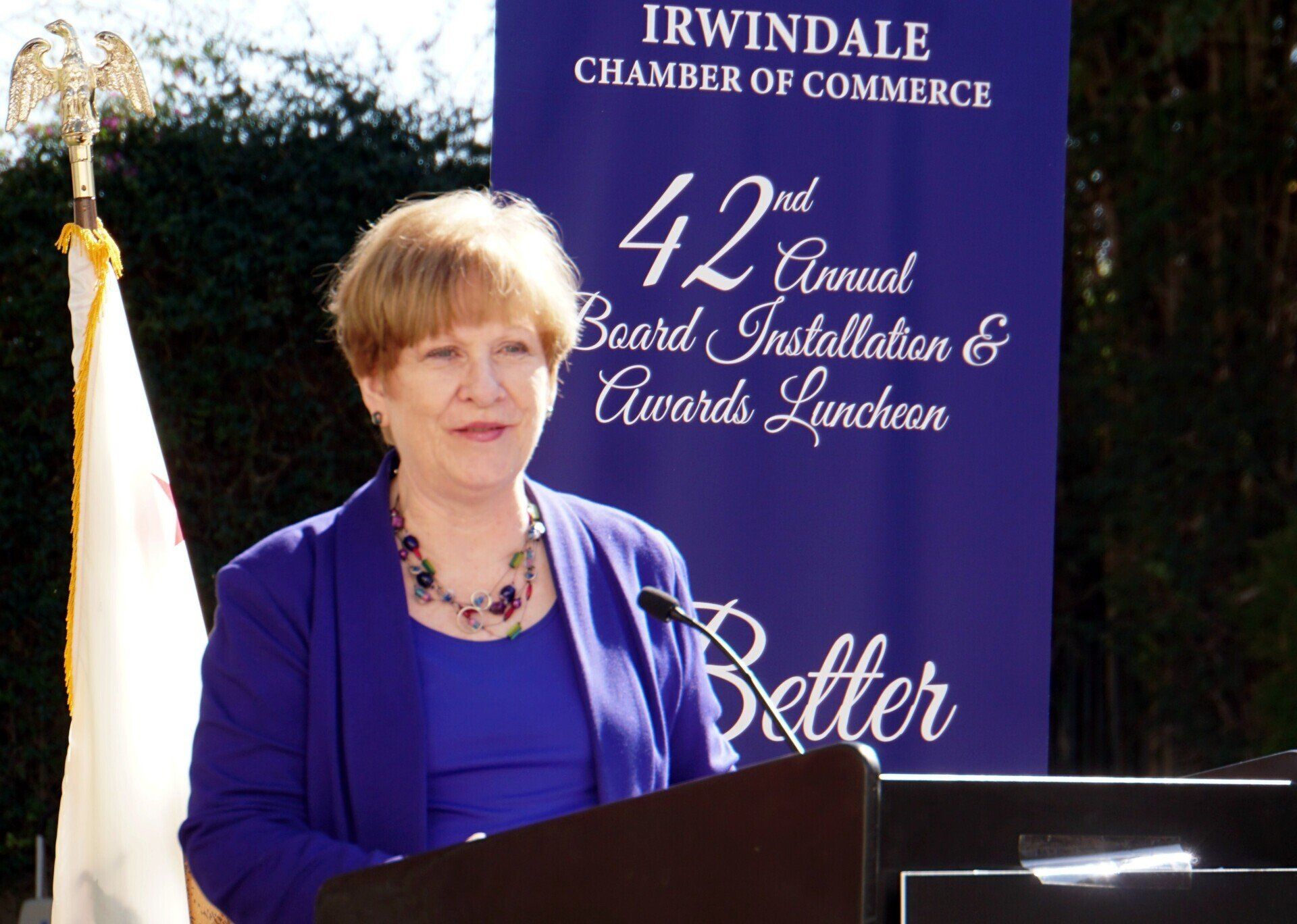 A woman stands at a podium in front of a sign that says irwindale chamber of commerce